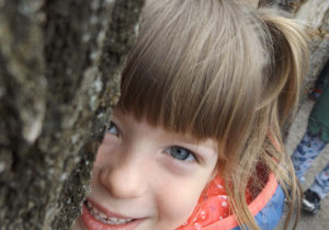 Dziewczynka podgląda zza drzewa.